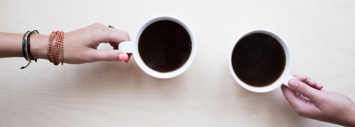 two hands holding white mugs with black coffee