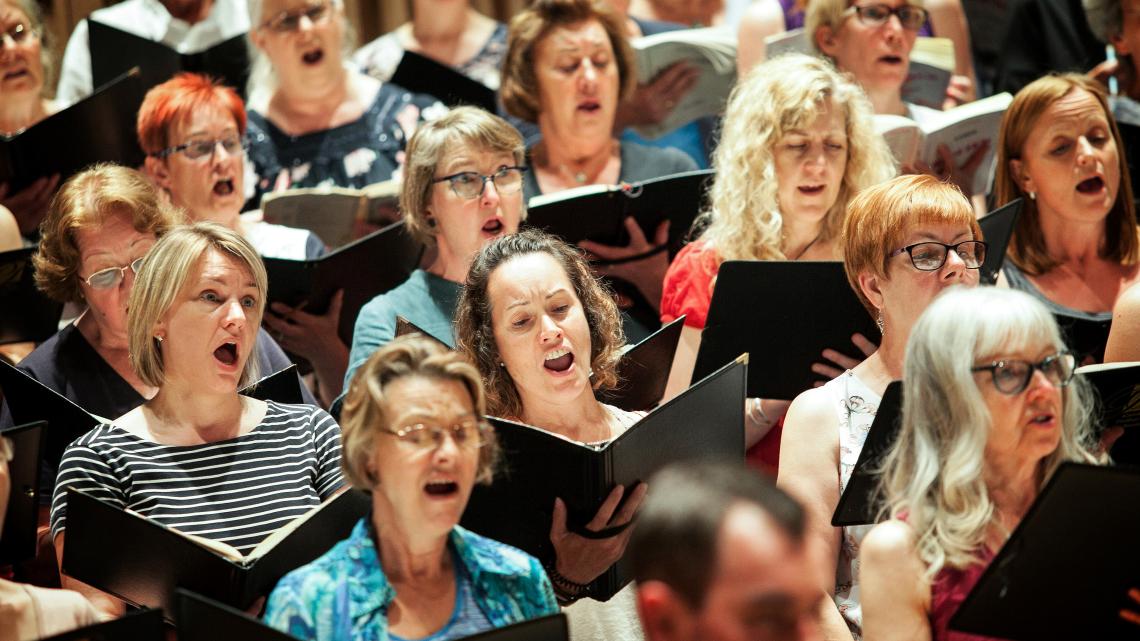 A group of women singing passionately whilst holding sheet music