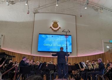 the two brass bands sitting on stage with their instruments, music director conducting, during the premiere