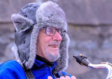 A member of Aberdeenshire Saxophone Orchestra smiles with his instrument, wrapped up warm for an outdoor rehearsal