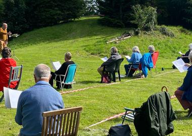 choir rehearses outdoors in green space with social distancing measures