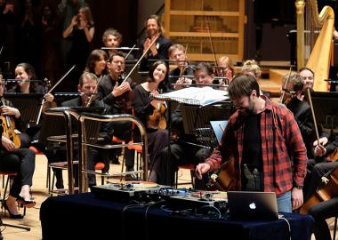 Mr Switch, a DJ, on stage with his turntable and DJ set, with the orchestra in the background