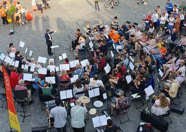 A group of musicians taking part in the Big Summer Wind Orchestra and Choir's Make Music Day 2023 event outside Kings Cross Station on a sunny day.