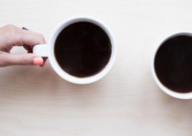 two hands holding white mugs with black coffee