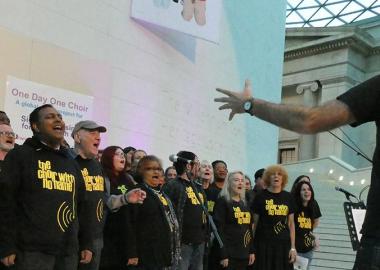 Choir With No Name wearing choir t shirts, singing in the British Museum Great Court, musical director conducting