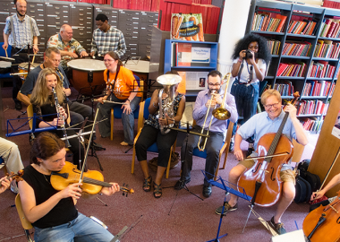 People gathered in a music library space playing orchestral instruments, smiling