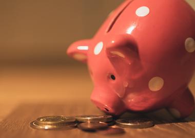 A pink piggy bank leaning over coins