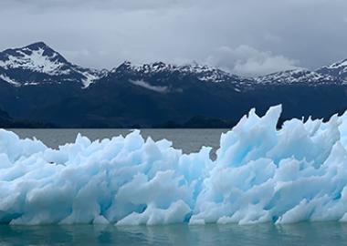 A small iceberg in water with a mountain backdrop