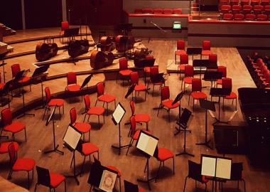 Red chairs and music stands are assembled onstage for an orchestra