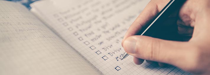 A hand holding a pen, poised over a notebook in which a checklist is written